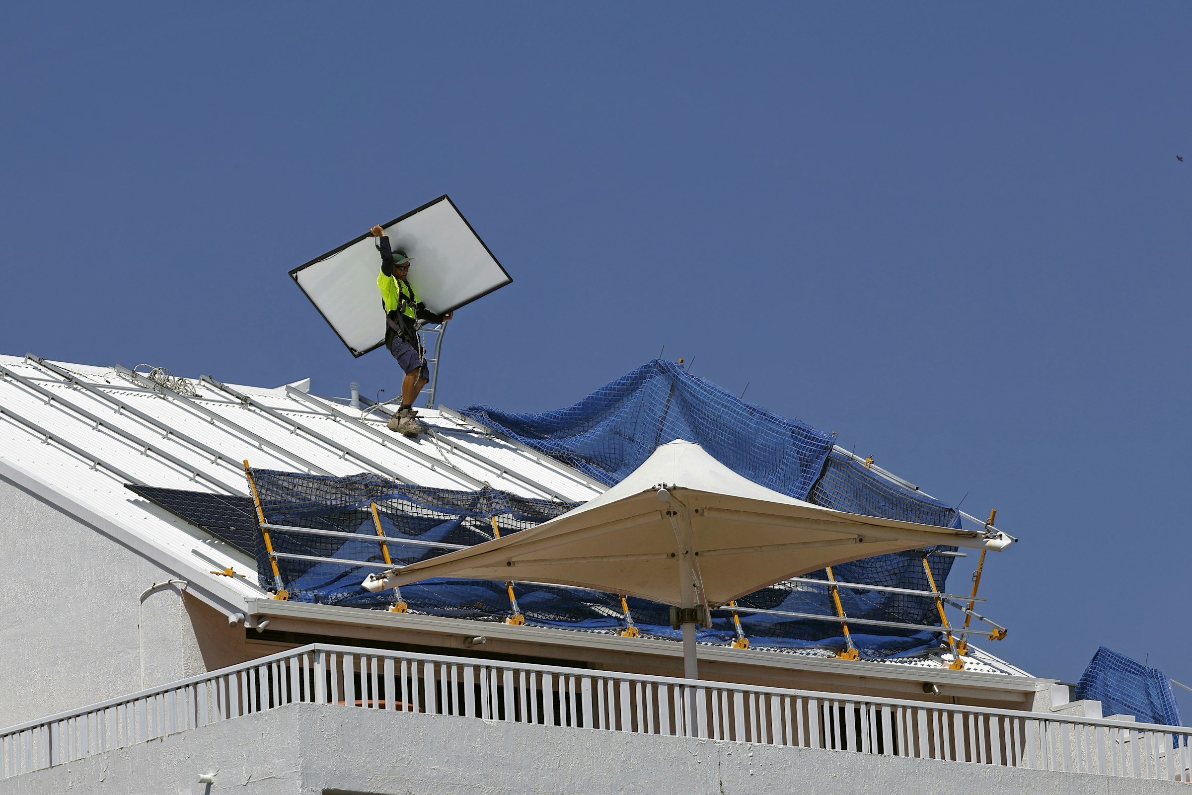 A worker carrying a solar module across a flat roof