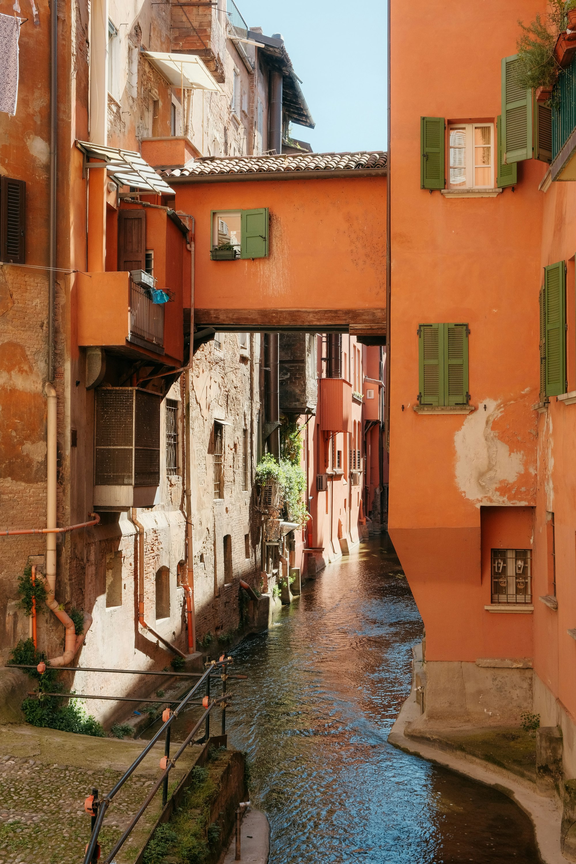 A narrow Bolognese street of ochre houses with green shutters, water running below